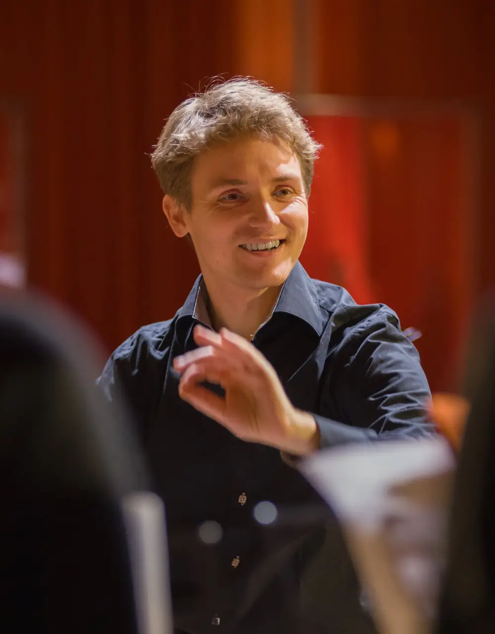 Der Dirigent Andreas Mitschke des Jazzchors leitet mit einer Handbewegung die Sängerinnen und Sänger und lächelt konzentriert.